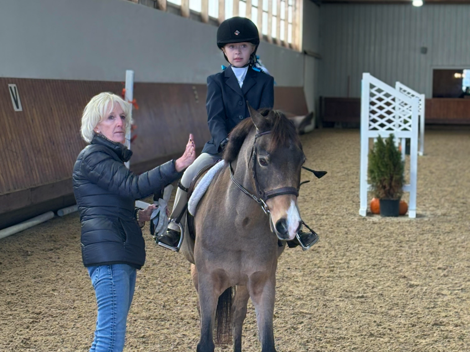 A trainer coaching a young rider on a buckskin pony in the indoor arena at Glen Eden